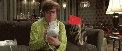 A Man In A Green Shirt Is Sitting On A Couch Holding A Shoe GIF