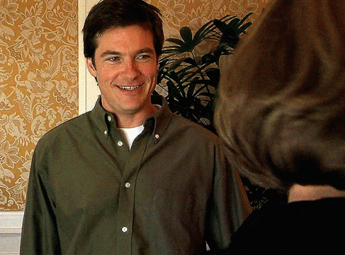 A Man In A Green Shirt Is Smiling While Talking To Another Person GIF