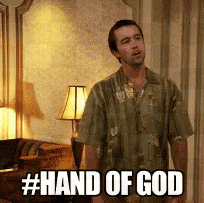 A Man In A Green Shirt Is Standing In A Living Room With The Words Hand Of God Written On The Screen . GIF