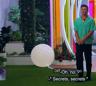 A Man In A Green Shirt Is Standing In Front Of A Colorful Wall And Says Let Oh No Go Secrets Secrets GIF
