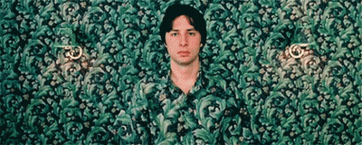 A Man In A Green Shirt Is Standing In Front Of A Wall GIF