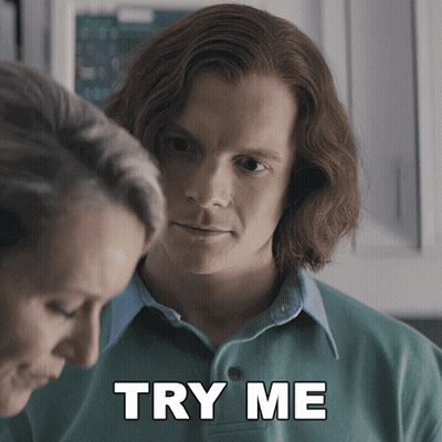 A Man In A Green Shirt Is Standing Next To A Woman With The Words Try Me Below Him GIF