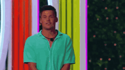 A Man In A Green Shirt Is Standing On A Stage In Front Of A Colorful Background . GIF