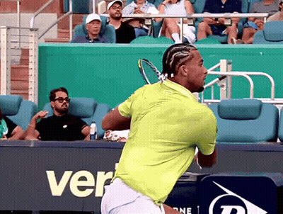 A Man In A Green Shirt Is Swinging A Tennis Racket In Front Of A Sign That Says Ver GIF