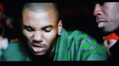 A Man In A Green Shirt Is Talking To Another Man In A Dark Room GIF