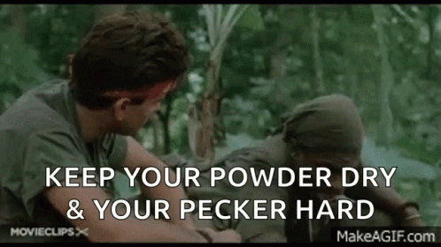 A Man In A Green Shirt Is Talking To Another Man In A Forest While Holding A Stick . GIF
