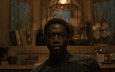 A Man In A Green Shirt Looks At The Camera In A Dark Room GIF