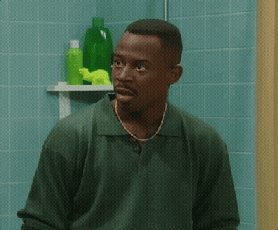 A Man In A Green Shirt Stands In Front Of A Bathroom Shelf With Green Bottles On It GIF