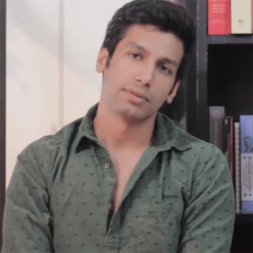 A Man In A Green Shirt Stands In Front Of A Book Shelf GIF