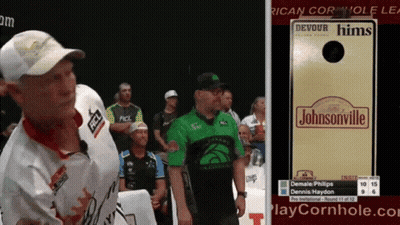 A Man In A Green Shirt Stands Next To A Sign That Says Johnsonville GIF
