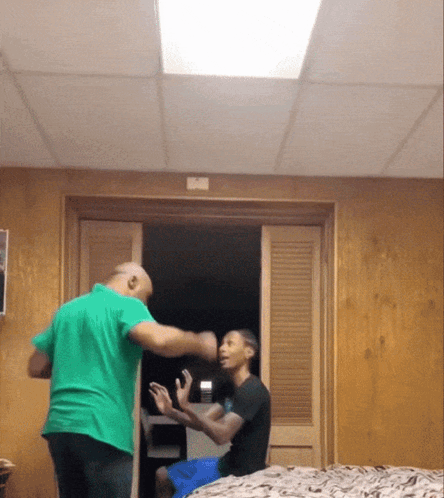 A Man In A Green Shirt Stands Next To Another Man In A Black Shirt GIF