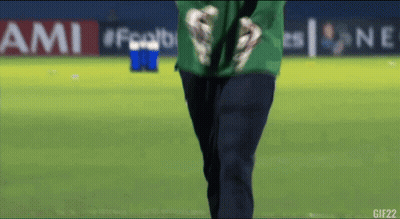 A Man In A Green Shirt Stands On A Soccer Field In Front Of An Ami Banner GIF