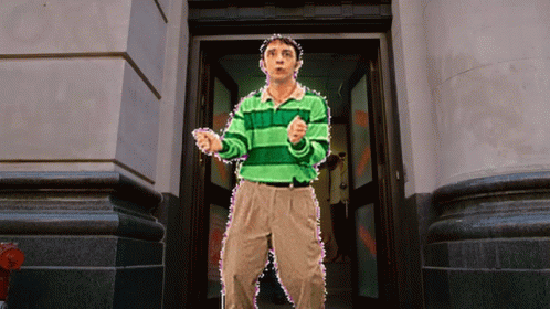 A Man In A Green Striped Shirt Is Standing In Front Of A Building GIF