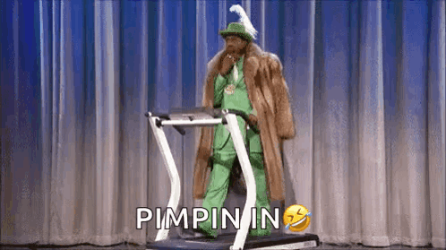 A Man In A Green Suit And Fur Coat Is Walking On A Treadmill . GIF
