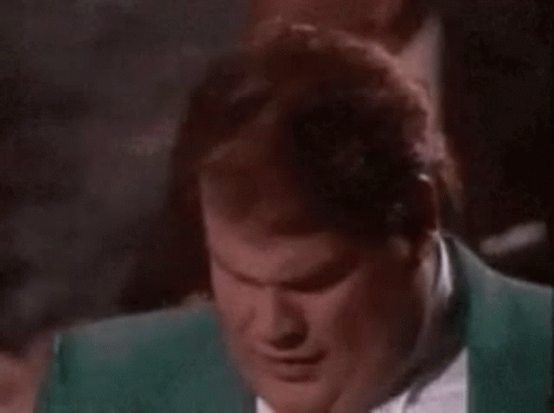 A Man In A Green Suit And Tie Is Smiling While Sitting In A Dark Room . GIF