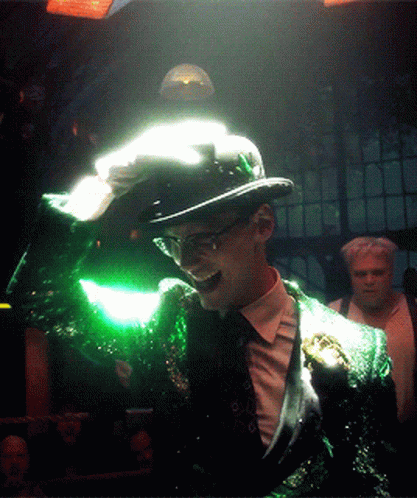 A Man In A Green Suit And Top Hat Is Holding A Green Object In His Hand GIF