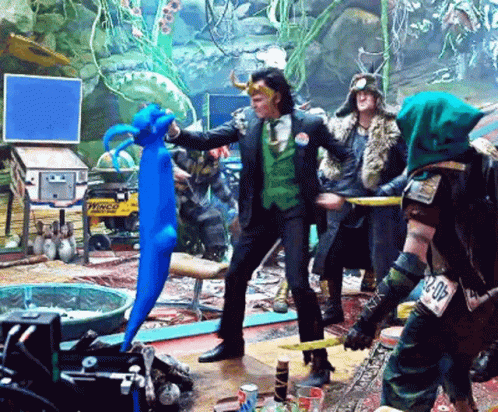A Man In A Green Suit Is Holding A Blue Stuffed Animal In A Room With Other People GIF
