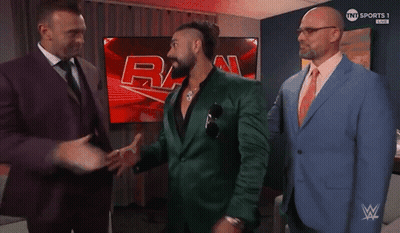 A Man In A Green Suit Talks To Two Other Men In Suits GIF