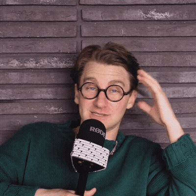 A Man In A Green Sweater Holds A Rode Microphone GIF