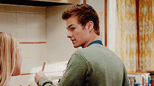 A Man In A Green Sweater Is Cooking In A Kitchen With A Woman Behind Him . GIF