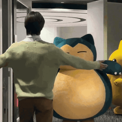 A Man In A Green Sweater Is Hugging A Stuffed Animal That Looks Like Snorlax GIF