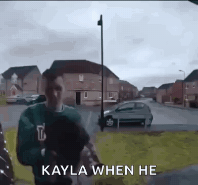 A Man In A Green Sweater Is Walking Down A Street With The Words `` Kayla When He '' Written On It . GIF