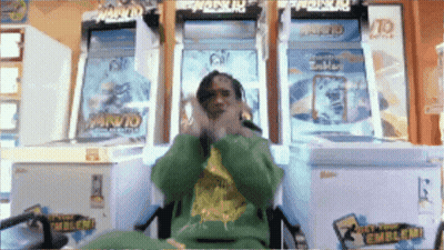 A Man In A Green Sweatshirt Is Sitting In Front Of A Naruto Game GIF