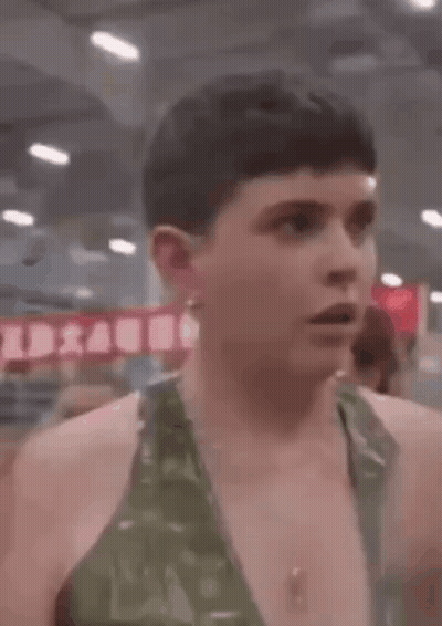 A Man In A Green Tank Top Is Standing In A Gym And Looking At The Camera . GIF