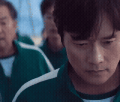 A Man In A Green Tracksuit Is Looking Down At Something While Standing In Front Of A Group Of People . GIF