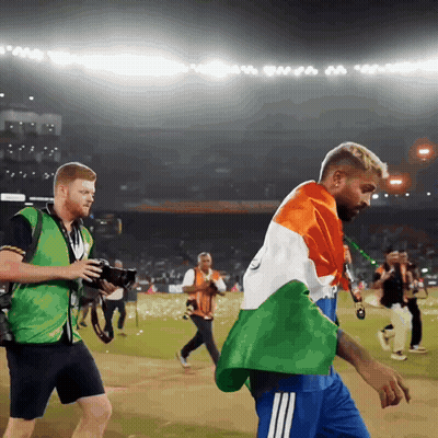 A Man In A Green Vest Is Taking A Picture Of Another Man In A Blue Shirt GIF