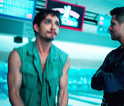 A Man In A Green Vest Stands Next To Another Man In Front Of A Bowling Alley GIF