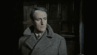 A Man In A Grey Coat Is Standing In Front Of A Door GIF