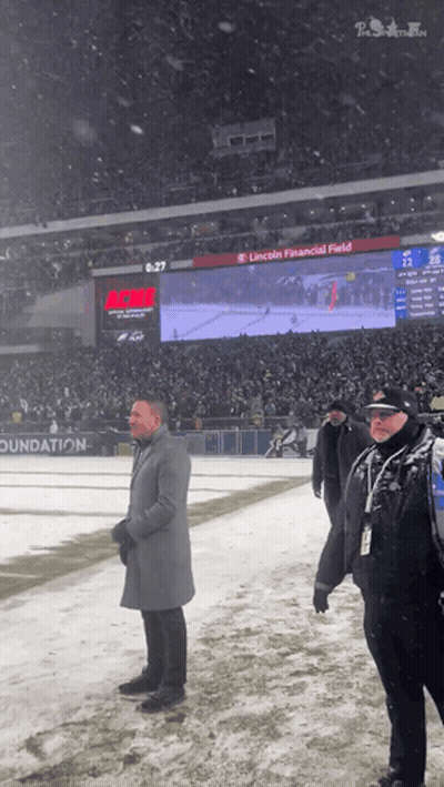 A Man In A Grey Coat Stands On A Snowy Field In Front Of A Scoreboard That Says Lincoln Financial Field GIF