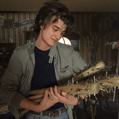 A Man In A Grey Jacket Is Holding A Bunch Of Sticks With Nails Sticking Out Of Them GIF