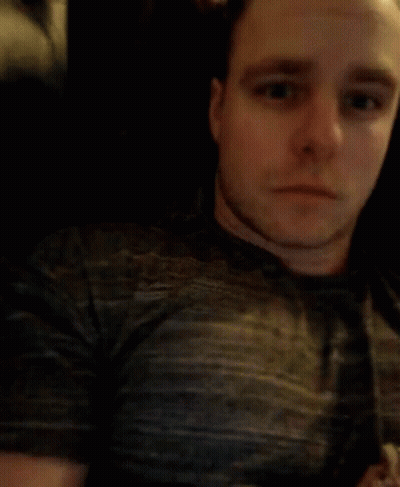 A Man In A Grey Shirt Is Blowing His Nose With A Tissue GIF
