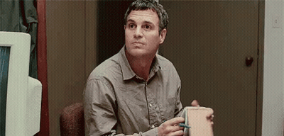 A Man In A Grey Shirt Is Sitting In A Chair Holding A Box And A Pen . GIF