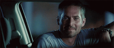 A Man In A Grey Shirt Is Smiling In A Car GIF
