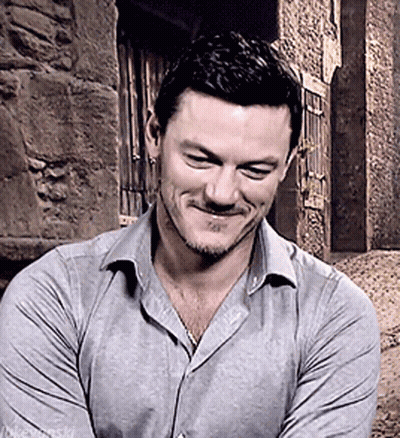 A Man In A Grey Shirt Is Smiling With His Arms Crossed In Front Of A Stone Wall GIF