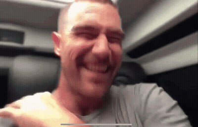 A Man In A Grey Shirt Is Smiling With His Eyes Closed In A Blurry Photo GIF