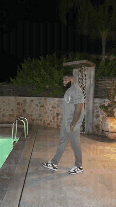 A Man In A Grey Shirt Is Walking By A Swimming Pool At Night . GIF