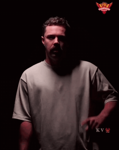 A Man In A Grey Shirt Stands In Front Of A Sign That Says Play With Fire GIF