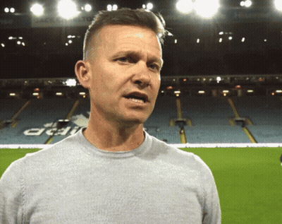 A Man In A Grey Shirt Stands In Front Of An Empty Stadium With A Sign That Says Acai On It GIF