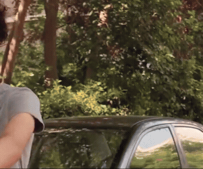 A Man In A Grey Shirt Stands Next To A Black Car GIF