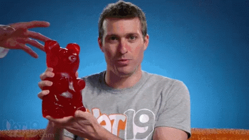A Man In A Grey Shirt With The Number 19 On It Holds A Large Gummy Bear GIF