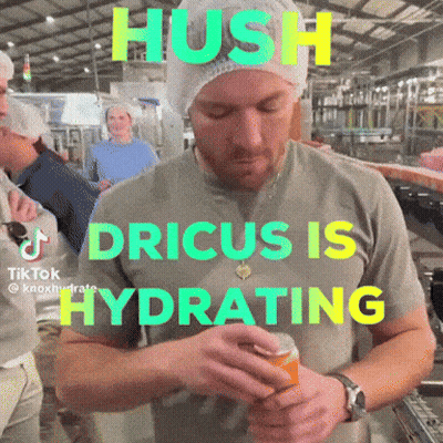 A Man In A Grey Shirt With The Words Hush Dricus Is Hydrating On The Front GIF