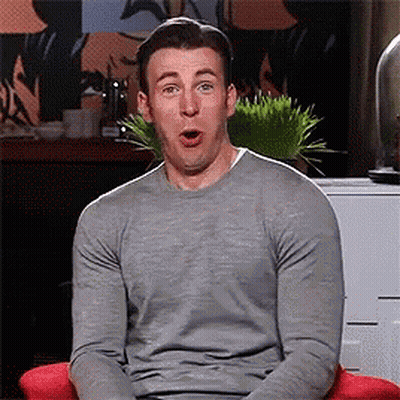 A Man In A Grey Sweater Is Sitting In A Red Chair With His Mouth Open . GIF