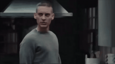 A Man In A Grey Sweater Is Standing In Front Of A Kitchen Hood GIF