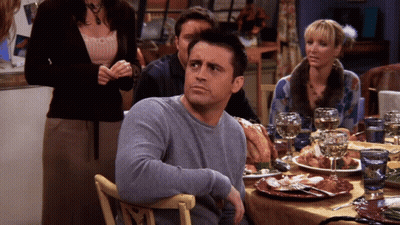 A Man In A Grey Sweater Sits At A Table With Plates Of Food GIF