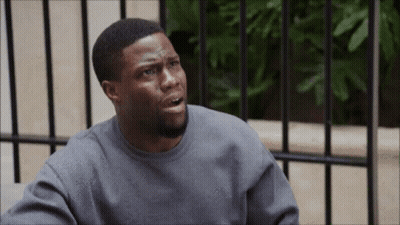 A Man In A Grey Sweatshirt Is Sitting In Front Of A Fence And Making A Funny Face GIF