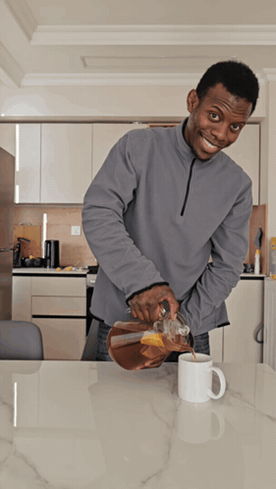 A Man In A Grey Sweatshirt Pours Coffee Into A White Mug GIF